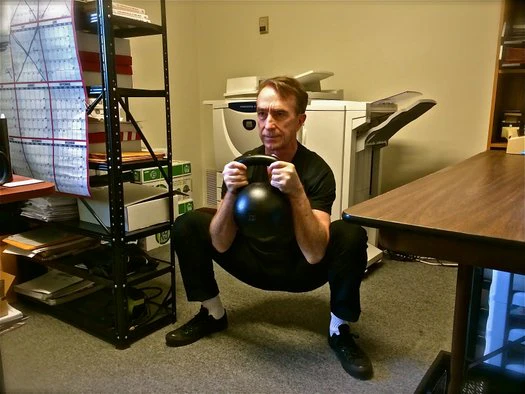 Büro-Workout John Du Cane führt einen 30 kg Goblet Squat im Dragon Door Büro aus
