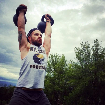 Bryan zeigt mobile Gelenke mit doppelten 24kg Kettlebells, die über Kopf verriegelt sind.